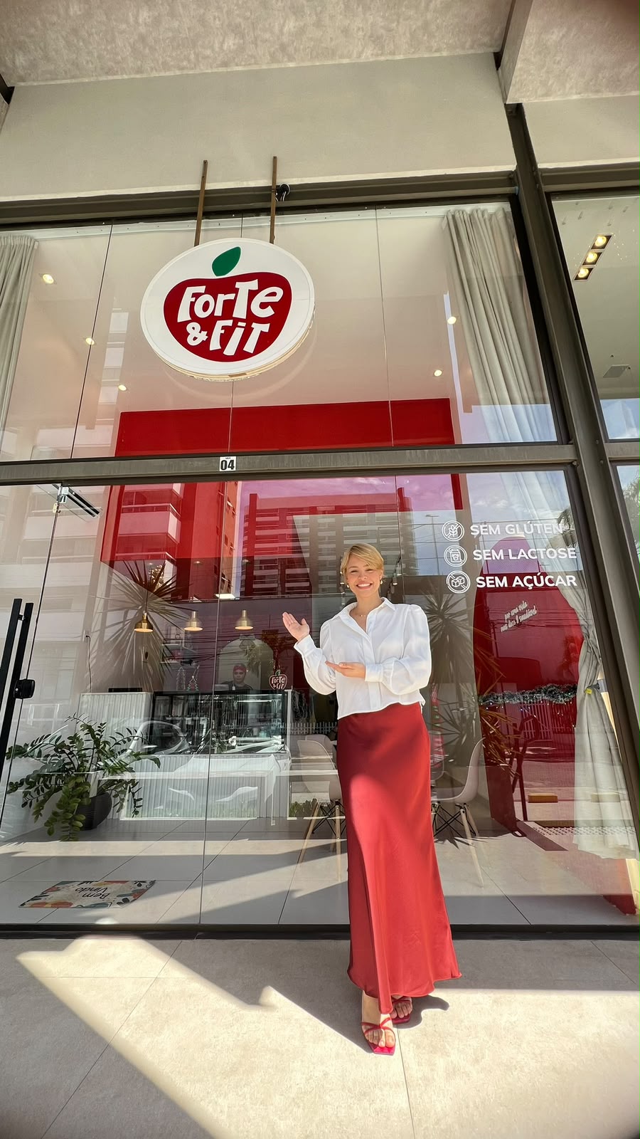 Gabriela Costa em frente à loja Forte e Fit, com a marca e a vitrine ao fundo